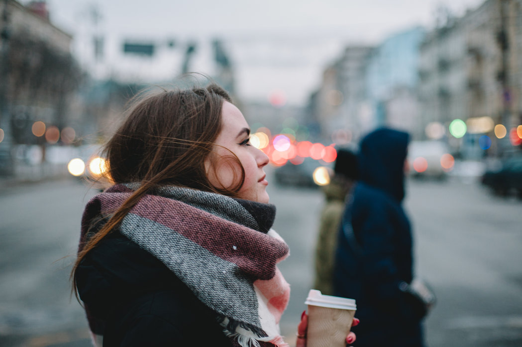 Woman with disposable cup in warm clothing crossing city street in winter