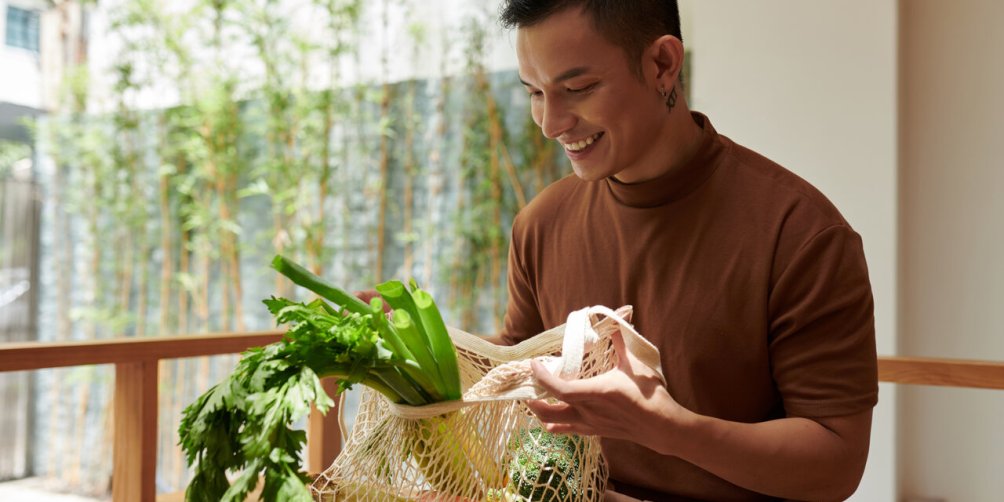 Happy young man taking out groceries he bought at local market