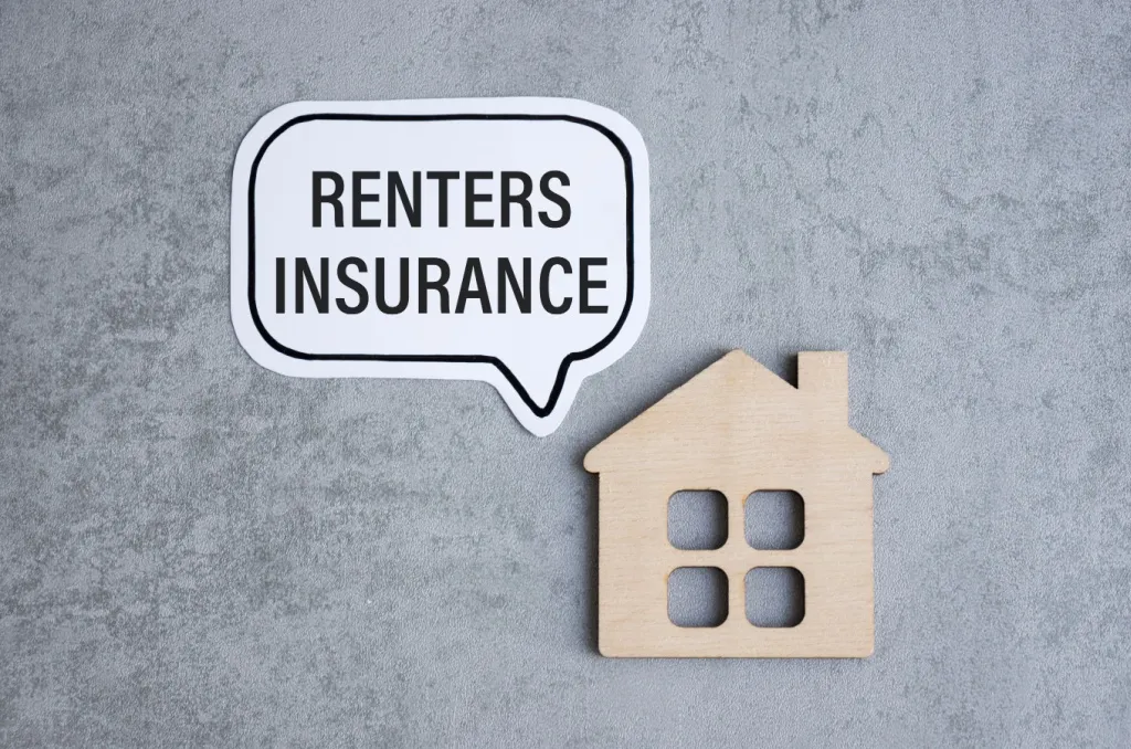 A white speech bubble with the words 'Renters Insurance' alongside a wooden house icon on a textured gray background.