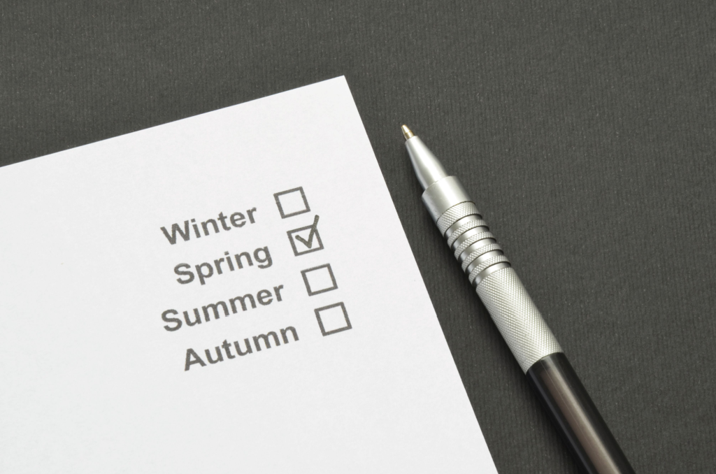 Cleaning checklist for seasonal organization with a marked checkbox for 'Spring' on white paper next to a silver pen.